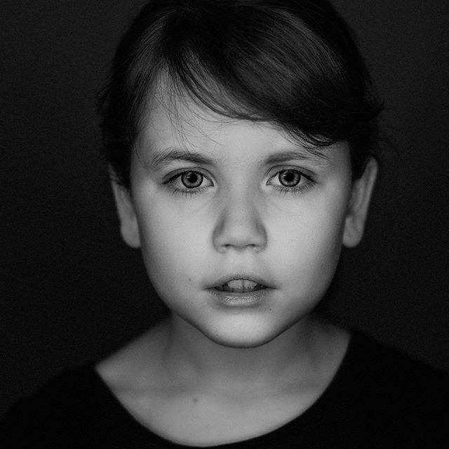 A monochrome, close-up portrait of a young girl with a serious expression against a dark background.