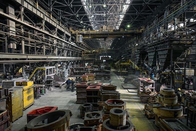 Inside a metal casting factory with workers and industrial equipment on the factory floor.