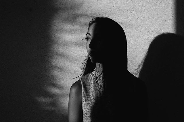 A woman stands in shadow against a textured wall, creating a moody and mysterious portrait.