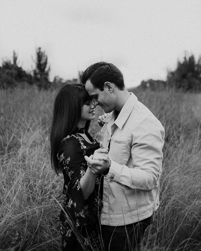 A couple embraces in a field, captured in an intimate black and white portrait.