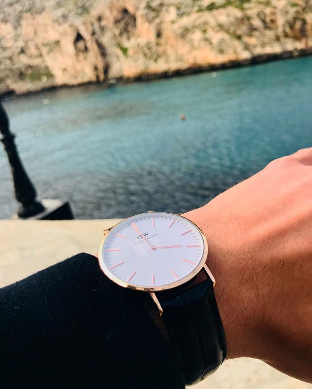 Close up of a stylish Daniel Wellington watch on a wrist against a scenic ocean backdrop.