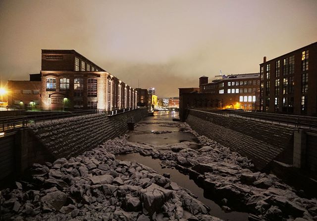Urban landscape at night featuring industrial buildings along a river, creating a peaceful and serene city scene.