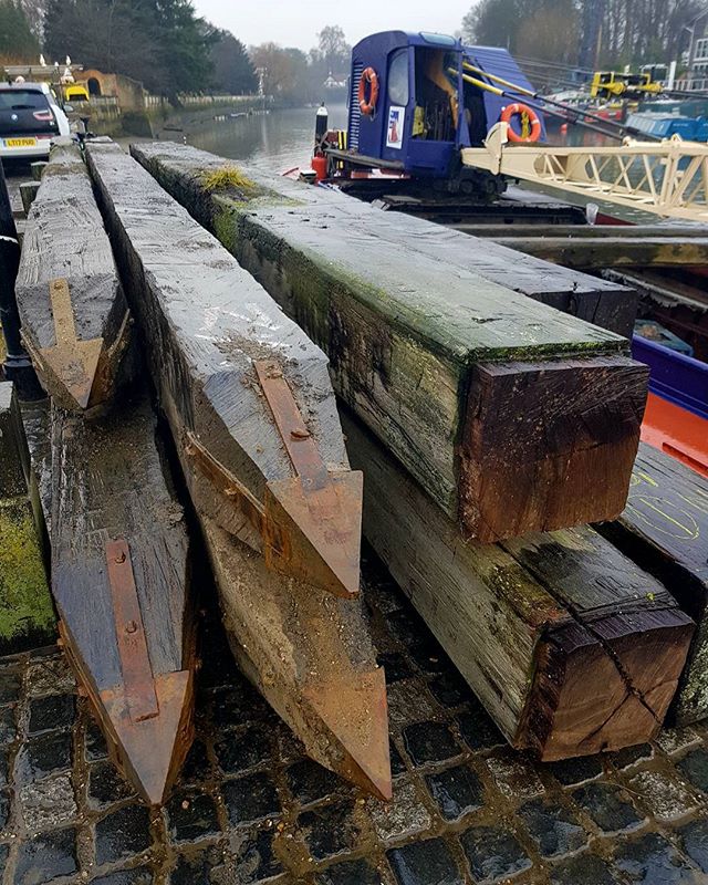 A collection of treated wooden pilings on a wet stone dock, ready for construction or renovation projects.