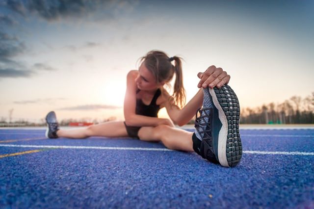 Female athlete stretching her legs on a blue track at sunset. Focused on fitness, flexibility, and a healthy lifestyle.