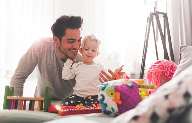 A father and baby girl are playing together with toys in a bright and happy living room setting.