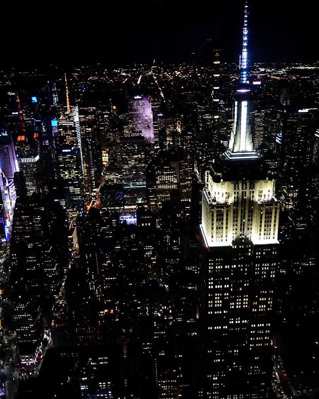 Night aerial view of New York City highlighting the illuminated Empire State Building and surrounding cityscape.