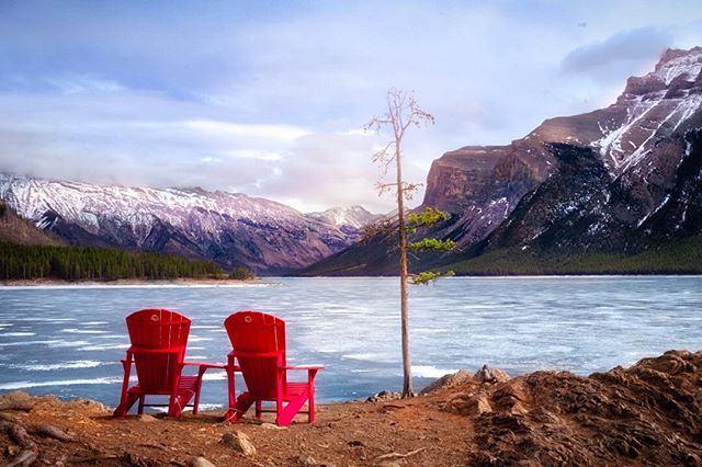 Two red chairs overlook a frozen lake nestled in a majestic mountain range on a tranquil, winter day.
