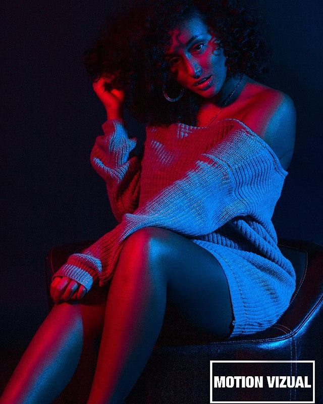 Stylish woman in a blue sweater poses in a studio, illuminated by red and blue lights for a captivating fashion editorial.