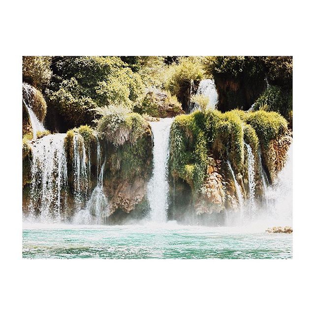 A scenic view of a cascading waterfall surrounded by lush greenery in a natural setting.