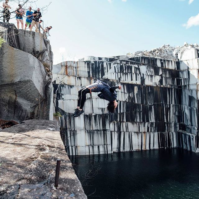 A cliff diver performs a backflip off a rocky cliff, showcasing adventure and extreme sports.