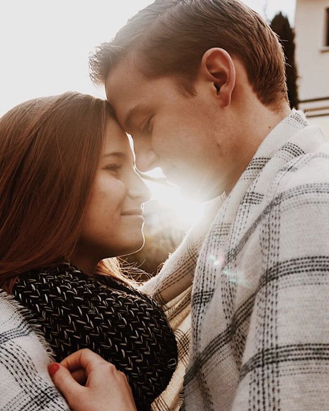 A couple shares a tender moment, wrapped in a blanket, bathed in the warm glow of sunlight.