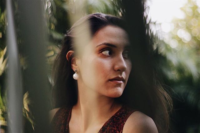 A serene woman gazes away in a soft, naturally lit outdoor portrait with a blurred background.