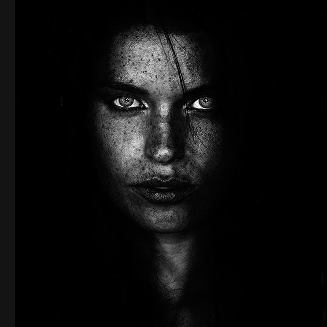A striking black and white portrait of a woman with freckles, captured with dramatic lighting and high contrast.