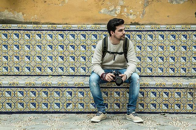 A photographer sits on a tiled bench, looking off to the side with a camera in his hand.