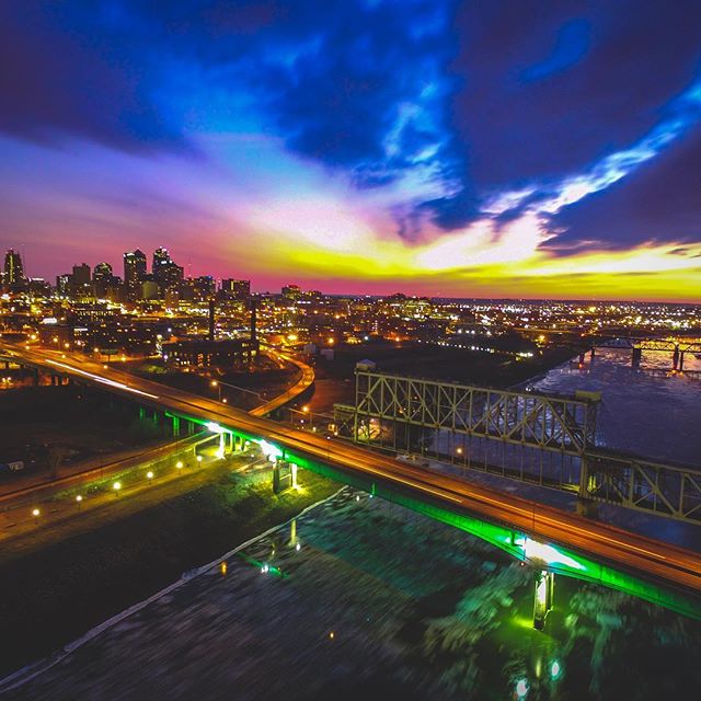 Nighttime cityscape featuring illuminated bridges, buildings, and a river under a colorful sky.