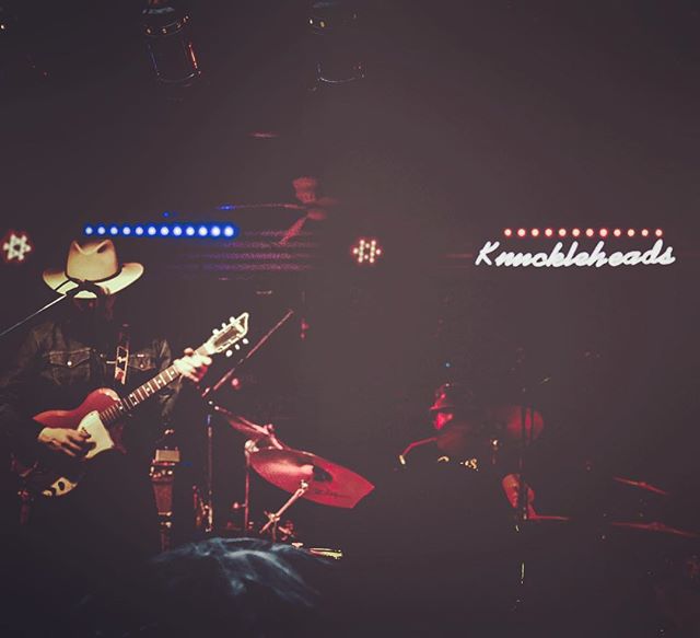 A musician in a cowboy hat performs with a drummer on stage at a concert.