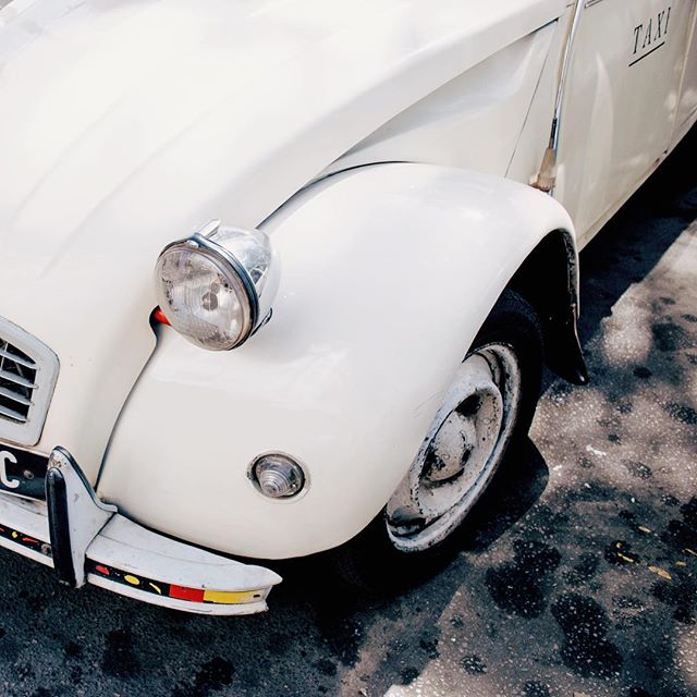 A vintage white Citroen 2CV taxi shows off its classic design in an urban setting.