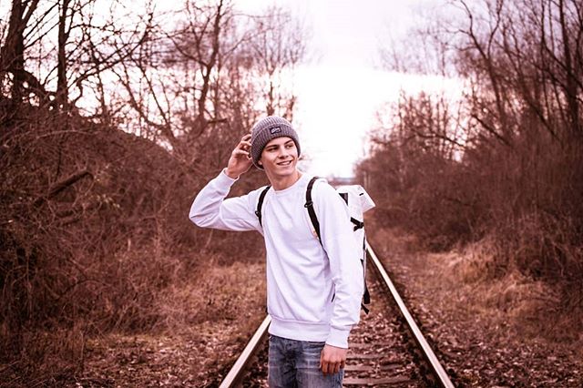 A young man with a backpack standing on railroad tracks in a natural setting.