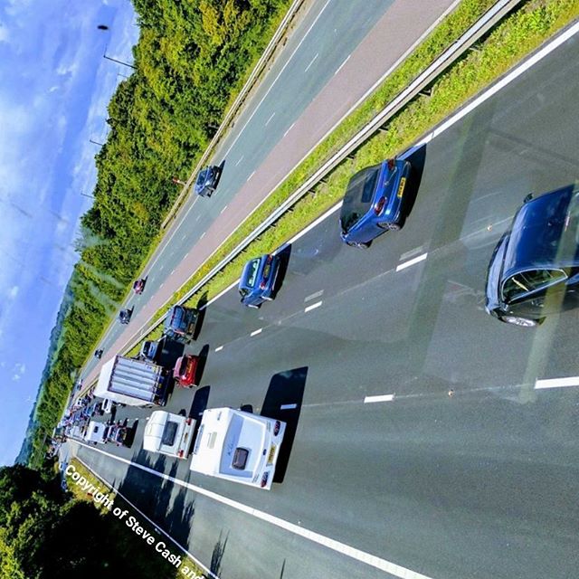 An overhead shot of cars and trailers travelling along a highway, showing a traffic jam on a sunny day.