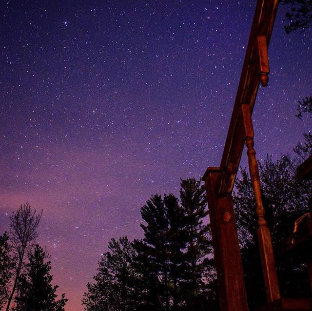 A beautiful view of the night sky filled with stars, framed by the wooden structure and silhouetted trees.