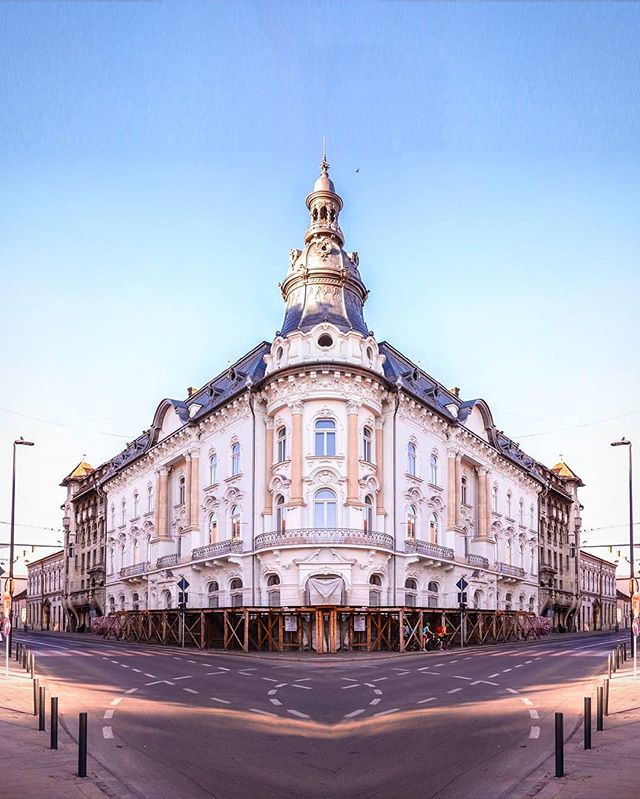 An ornate building with a tower stands at a street corner in a city, showcasing classic European architecture.