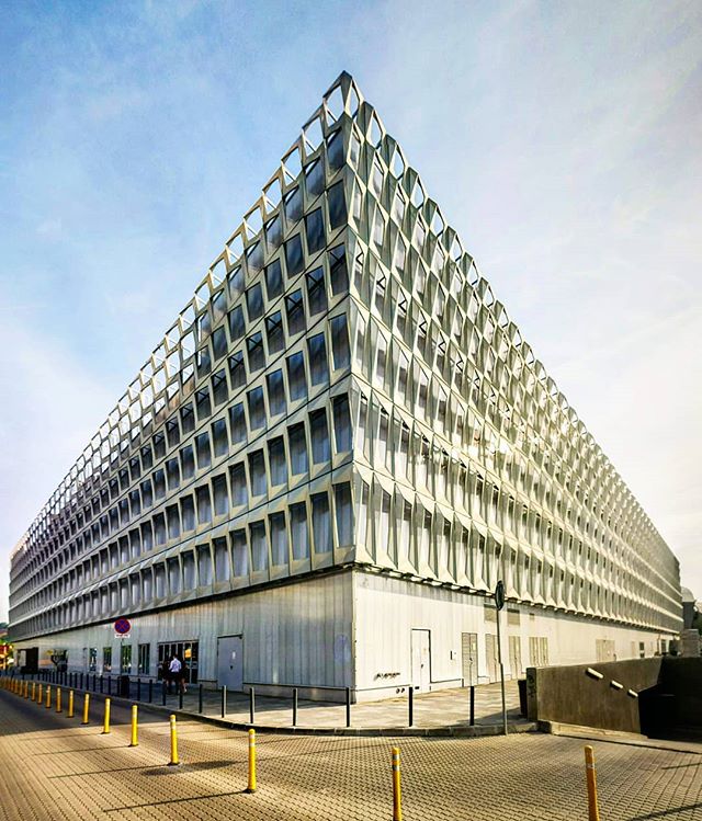 A modern, geometric building stands prominently against a blue sky in an urban setting.