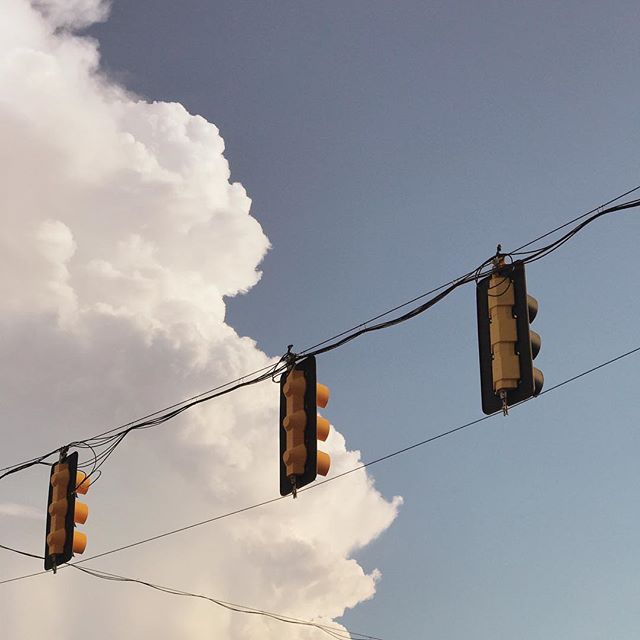 Three traffic lights hang against a cloudy sky on powerlines in a calm outdoor setting.