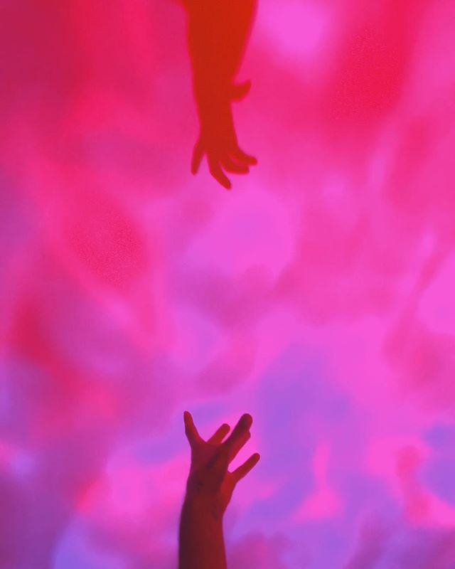 Two hands reach towards each other against a vibrant pink and purple background.