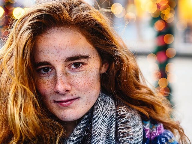 Portrait of a woman with red hair and freckles wearing a scarf, with bokeh lights in the background.