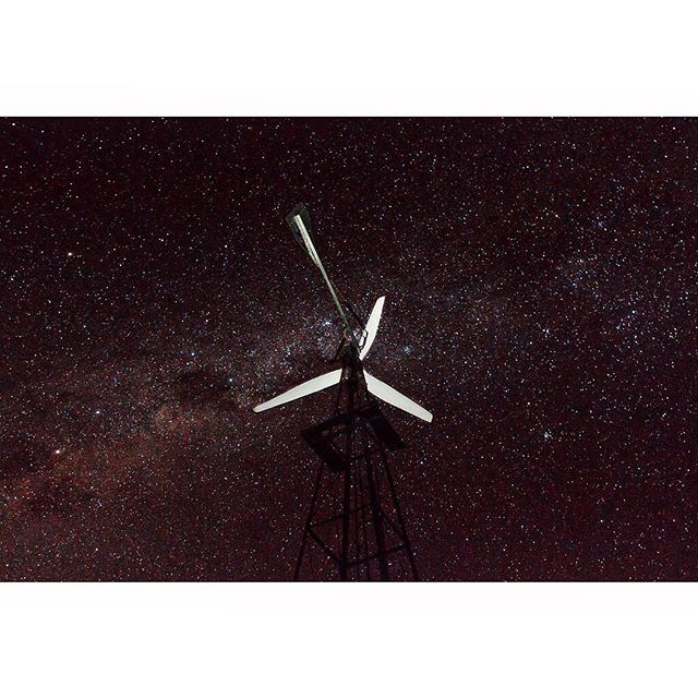 A silhouette of a windmill set against a stunning, star-filled night sky. The night sky is a celestial display of stars.