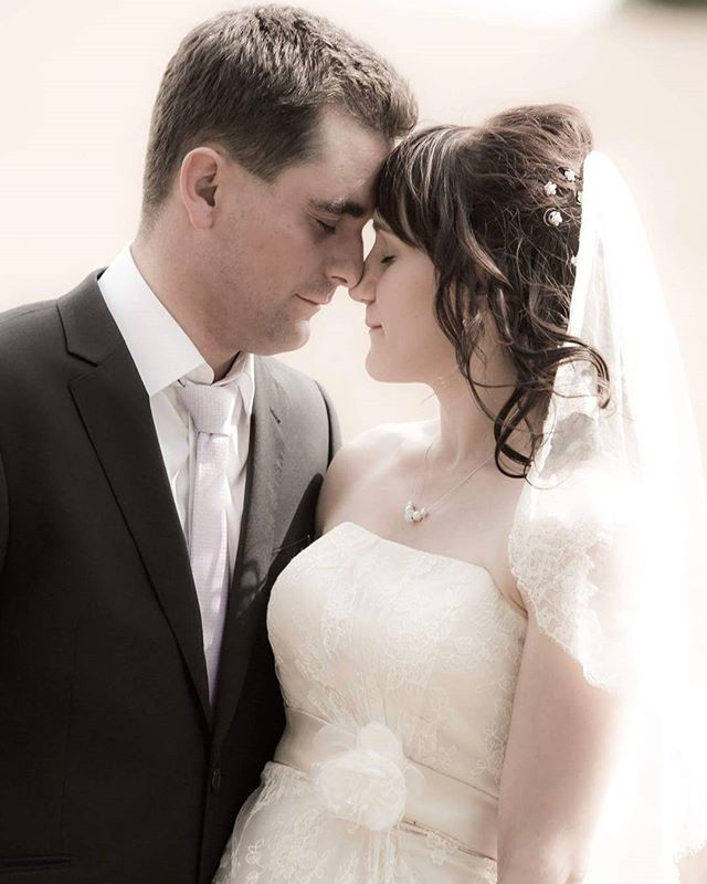 A bride and groom share a tender moment, foreheads touching, in a romantic outdoor setting.