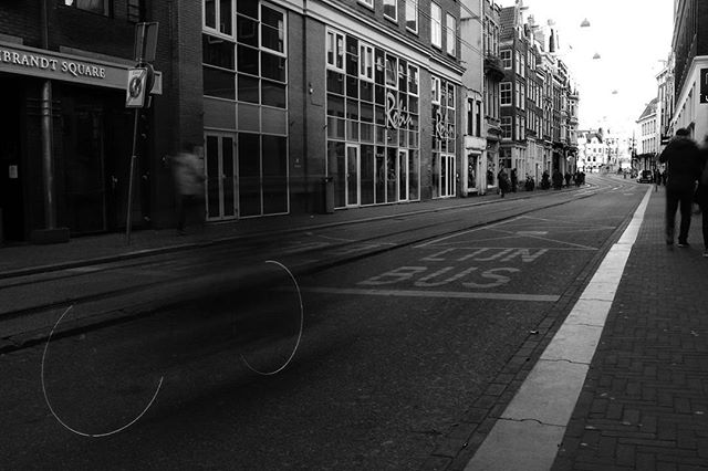 A black and white cityscape shows a European street with buildings and people captured using long exposure for motion blur.
