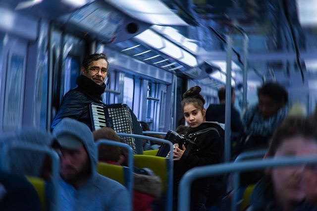 A man and a girl play accordion on a crowded subway car. The scene reflects urban life and public transport.