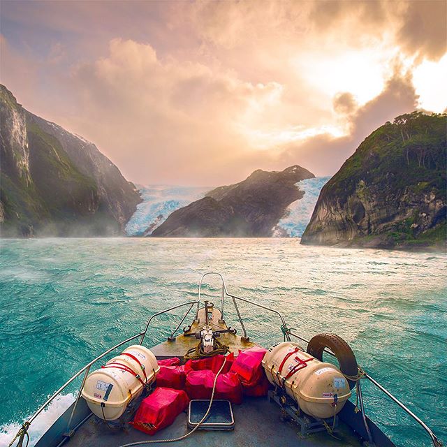 Breathtaking view of a glacier meeting the sea, captured from a boat sailing through a tranquil fjord surrounded by mountains.