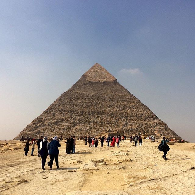 The Great Pyramid of Giza stands tall against a blue sky as people explore this iconic ancient wonder in the Egyptian desert.