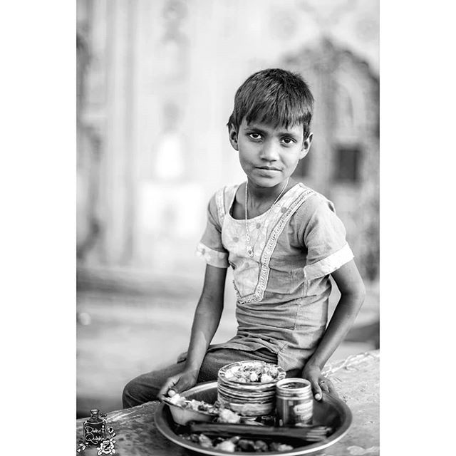 A young boy sits holding a tray of food, capturing a moment of daily life in black and white.