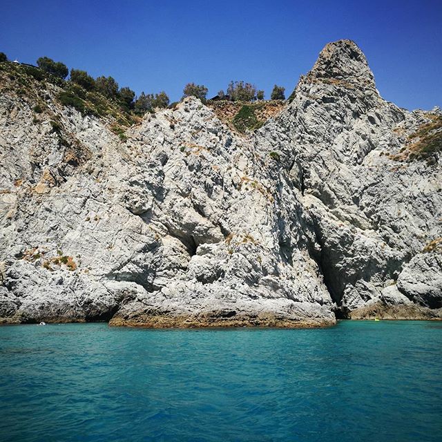 A striking rock formation juts out of the turquoise sea under a clear blue sky, a beautiful coastal scene.