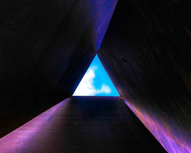 A low-angle view through a triangular structure reveals the sky, blending modern architecture with natural elements.