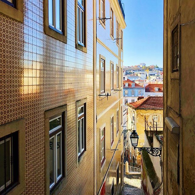 A charming narrow street in Lisbon, Portugal, featuring traditional buildings and a glimpse of the cityscape beyond.