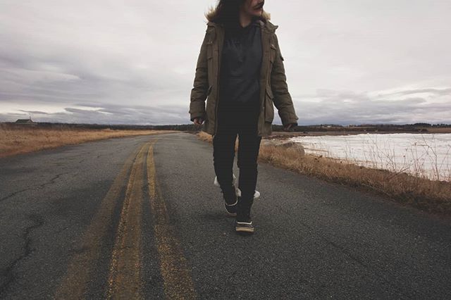 A person in a parka walks on a rural road under a cloudy sky, showcasing a peaceful outdoor lifestyle.