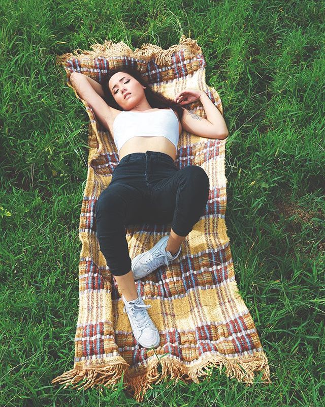A woman relaxes on a blanket in the grass, enjoying a peaceful outdoor moment.