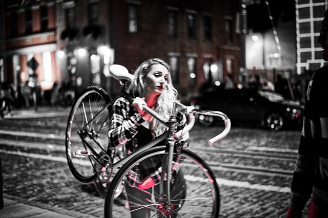 A woman carries a bicycle on a city street at night, illuminated by selective red lighting for a moody feel.