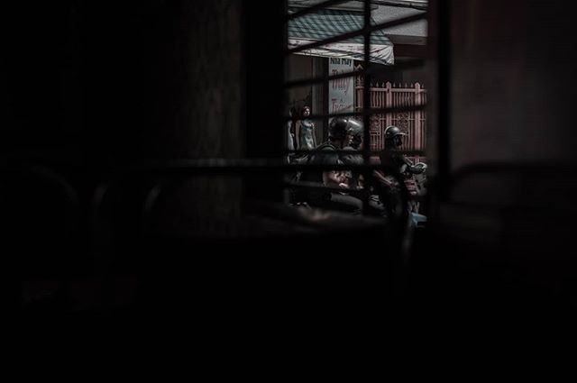 A view through a window shows people on motorcycles in an urban street scene.