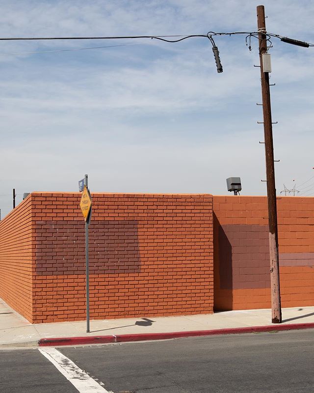 A brick wall with a street sign and telephone pole under a bright sky in an urban setting.