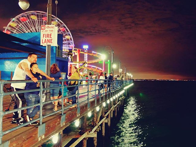 People enjoy the vibrant night scene at a pier with a Ferris wheel in the background.
