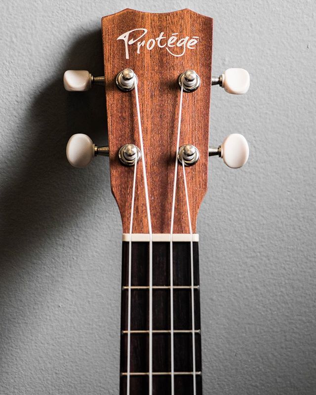 A close-up shot of a ukulele's headstock and fretboard shows the instrument's details and craftsmanship.