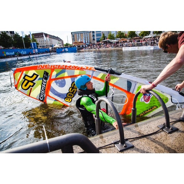 A windsurfer in the water with a vibrant sail is helped out of the water during a competition.