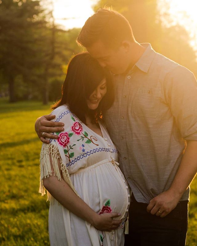 A pregnant woman and a man embrace tenderly in a sunlit park, showcasing love and anticipation.