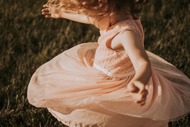 A young girl twirls in a pink dress, enjoying a sunny day in a grassy field.