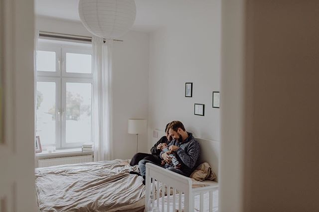 A family with a newborn baby is sitting on a bed in a bright, airy bedroom at home.